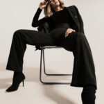 Portrait beautiful woman with attitude sitting on a chair wearing black clothes posing on white background looking at the camera